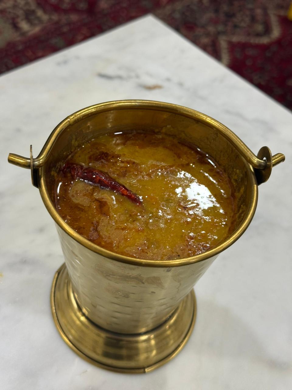 Dal in a brass bucket, topped with a whole dried red chilli