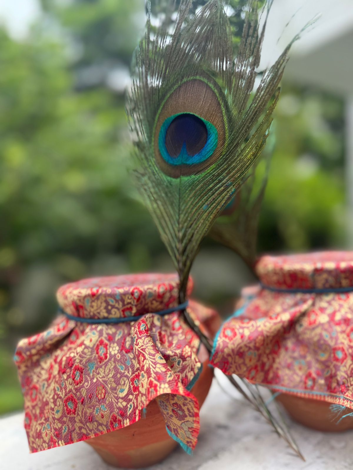 Two matkis of makhana kheer side by side, each sealed with brocade and a peacock feather